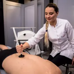Fizjoterapeutka wykonuje kriolezję stawu biodrowego u pacjenta leżącego na kozetce.