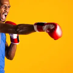 A boxer in a blue tank top throws a punch, his face contorted in a roar. He's ready to compete in the junior welterweight weight class.