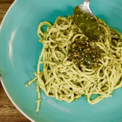 Un plato de pasta al pesto, con una cuchara añadiendo más salsa verde.