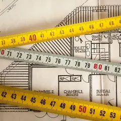 Cintas métricas sobre planos de construcción, ilustrando la diferencia de metros entre registro de propiedad y catastro.