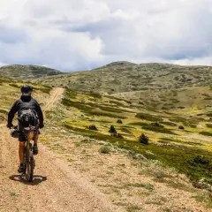 Ciclista pedaleando por un camino de tierra en **montañas vacías** bajo un cielo nublado.