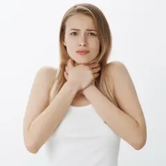 Młoda kobieta z wyrazem niepokoju na twarzy ściska sobie gardło. Czuje flegmę po jedzeniu.