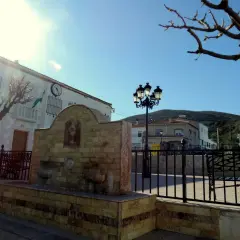 Fuente de piedra en Chercos, Almería, con un edificio blanco y un reloj al fondo.