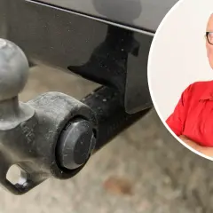 En man i röd tröja med texten "Tekniker Värld" ler. Bredvid syns en dragkrok, kanske för en besiktning.