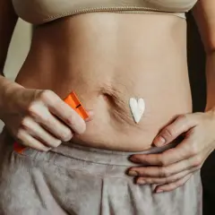 Krem w kształcie serca na brzuchu, pokazujący jak ujędrnić skórę. Kobieta trzyma tubkę z kosmetykiem.