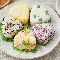 A colorful assortment of musubi vs onigiri, each a unique rice ball shape with various toppings like peas, seaweed, and cucumber.