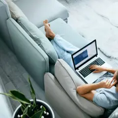 Mężczyzna relaksuje się na kanapie, pracując na laptopie. W tle widać roślinę doniczkową. To idealne miejsce do pracy zdalnej, jak na platformie ozzion.