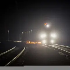 Nocny tor kolejowy rozświetlony reflektorami pociągu i iskrami z prac na torach.