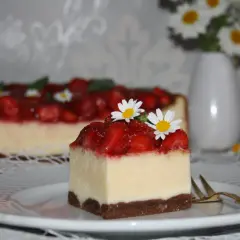 Pyszny sernik z truskawkami, udekorowany świeżymi kwiatkami, kusi swoim wyglądem.