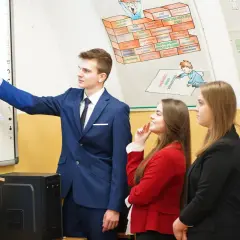 Młody technik ekonomista tłumaczy wykres na tablicy interaktywnej grupie uczniów.