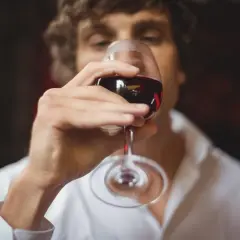 Un homme déguste un verre de vin rouge, savourant le langage du vin.