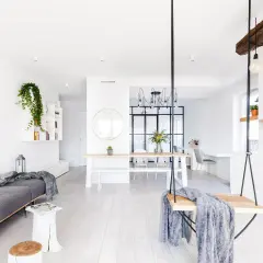 Jasny salon z białymi ścianami, szarą kanapą, huśtawką i stołem jadalnianym.