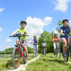 Familie genießt das **Radfahren mit Kindern** auf einem sonnigen Weg am See.