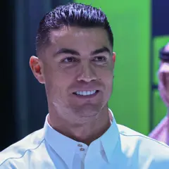 Cristiano Ronaldo w białej koszuli, uśmiecha się. W tle mężczyzna w tradycyjnym arabskim stroju.