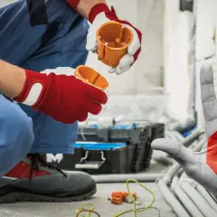 Elektryk montuje puszkę, a dłoń z symbolem stopu ostrzega: czy prąd może uciekać w ścianę? Uważaj na instalację!