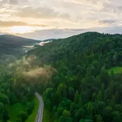 Mgła snuje się nad zielonymi dolinami, a kręta droga wije się przez gęste lasy. Bieszczady góry budzą się do życia o wschodzie słońca.
