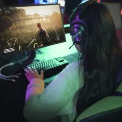 Dziewczyna w słuchawkach gra w grę fps na komputerze. Wirtualna przygoda wciąga ją bez reszty.
