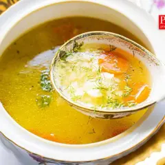 A ladle lifts a spoonful of the **najlepsza zupa ryżowa**, revealing tender rice, carrots, and dill in a golden broth.