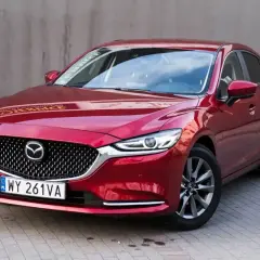 Czerwona Mazda 6 2.0 benzyna zaparkowana na kostce brukowej. Elegancka linia nadwozia i charakterystyczny grill.