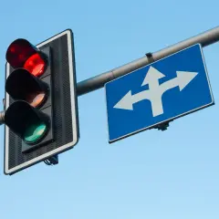 Migające światła na przejeździe kolejowym wskazują, że zbliża się pociąg. Znak pokazuje, że można jechać prosto lub skręcić.