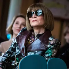 Anna Wintour w okularach przeciwsłonecznych i wzorzystej kurtce, ikona Vogue, wpatruje się w dal.