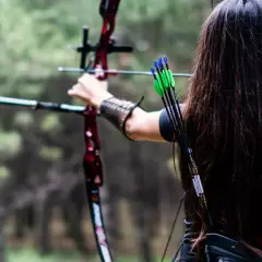 Łuczniczka celuje z łuku bloczkowego, jednego z wielu rodzajów łuków. Strzały w kołczanie mają zielone lotki.