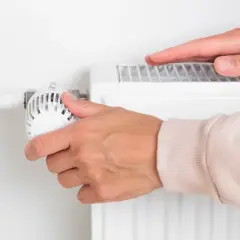 Dłoń reguluje termostat grzejnika, zastanawiając się, kiedy wyłączyć ogrzewanie w domu, by oszczędzić energię.