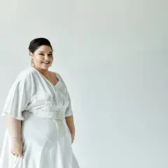 Uśmiechnięta panna młoda w pięknej, białej sukience weselnej plus size z ozdobnym pasem.