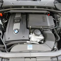 Silnik BMW E90. Widoczny jest czarny, plastikowy kolektor dolotowy, pokrywa silnika z logo BMW i oznaczeniem M, a także zbiornik płynu chłodniczego.