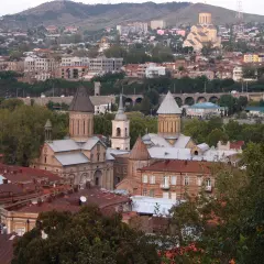 Widok na Tbilisi, gdzie zabytkowe cerkwie i domy z czerwonymi dachami opowiadają historię Gruzji. W tle widać wzgórza i nowoczesne budynki.