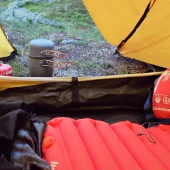 Czerwony śpiwór puchowy czy syntetyczny? Wnętrze namiotu z materacem, menażką i butlą gazową.