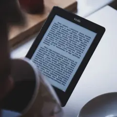 Une personne lit sur une liseuse Kindle. L'écran affiche du texte, suggérant une lecture immersive. Idéal pour partager livre kindle.