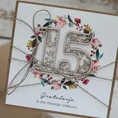 Elegancka kartka z napisem "Gratulacje W dniu Waszego Jubileuszu" i ażurową liczbą "15", ozdobiona wianuszkiem z kwiatów i liści. Idealna na kryształową rocznicę.