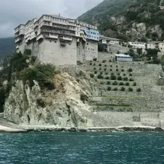 Monastyr na Athos, zbudowany na skalistym zboczu, z tarasowymi ogrodami i widokiem na morze.