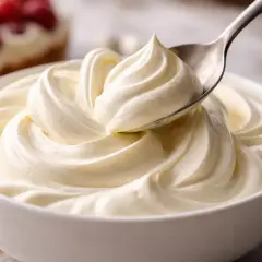Une cuillère prélève une portion de chantilly mascarpone onctueuse dans un bol blanc. Des fruits rouges sont visibles en arrière-plan.