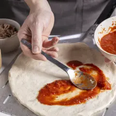Zubereitung eines italienischen Thunfisch Pizza Rezepts: Tomatensauce wird auf den Teig gestrichen. Daneben liegen Thunfisch und Käse.
