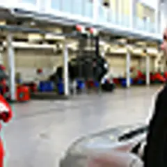 Mechanik w czerwonym kombinezonie omawia z klientem kwestie związane z ekologicznym paliwem, takim jak biodiesel, w warsztacie samochodowym.