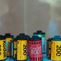 A collection of various types of 35mm film rolls, including Kodak 200, Kodak 400, and CineStill 800T, are displayed.