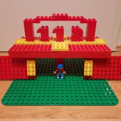 Ein kleiner Junge steht unter einem roten und gelben LEGO Duplo Tor, das wie eine Feuerwache aussieht. Die Zahl 112 ist darauf abgebildet.