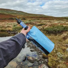 Vattenrening vandring: en hand håller en Sawyer vattenfilterpåse vid en bäck i fjällterräng.