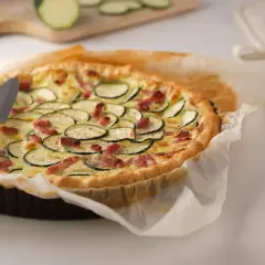 Une délicieuse quiche courgette lardon dorée, garnie de rondelles de courgettes et de lardons croustillants, prête à être dégustée.