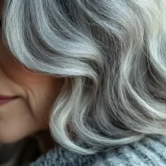 El cabello plateado de una mujer, con ondas suaves, muestra la belleza natural de porque salen las canas.