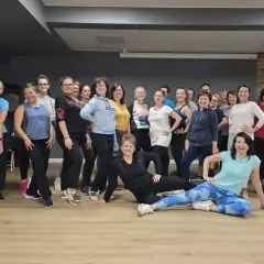 Grupa kobiet na zajęciach nauka tańca, uśmiechnięte, w sportowych strojach, pozują do zdjęcia.