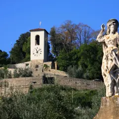 Statua di santo e torre dell'orologio su una collina verdeggiante, un'immagine che cattura l'essenza di cosa vedere ad Artimino.