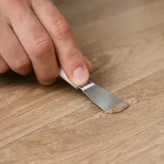 Mano che applica stucco per la riparazione parquet su una fessura del legno.