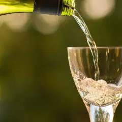 Un vin blanc pétillant est versé dans un verre, créant une mousse légère qui rappelle le sucre dans le vin.