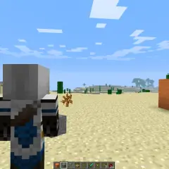 Postać w grze Minecraft stoi na pustyni, obok niej widać mechanizm z pomarańczowych bloków i czerwonego proszku.