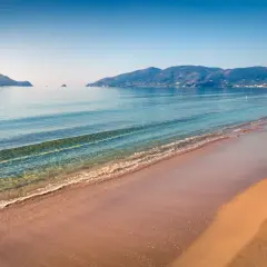 Spokojne morze obmywa piaszczystą plażę Kalamaki. W oddali widać zielone wzgórza i małe wysepki.