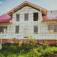 Budowa domu z białych pustaków, z czerwonym dachem i zakrytymi oknami.