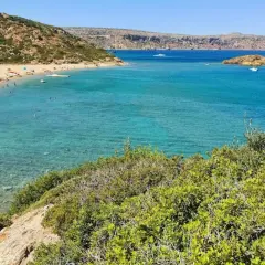 Słoneczna plaża Vai z turkusową wodą, zielonymi wzgórzami i ludźmi relaksującymi się na piasku.